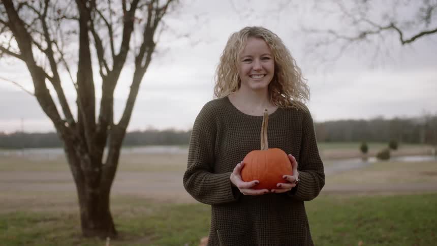 A woman holds a small orange pumpkin