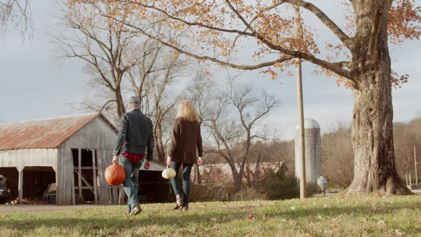 Man and woman walk towards a barn carrying pumpkins