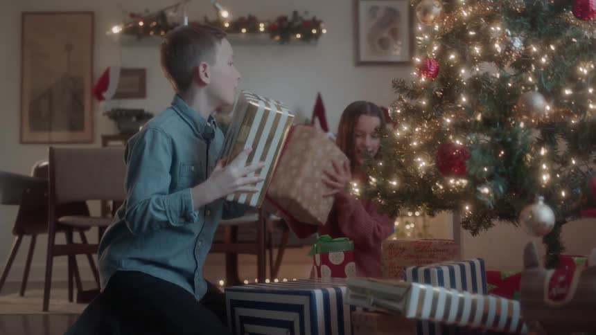 Boy and girl look at presents beneath a christmas tree