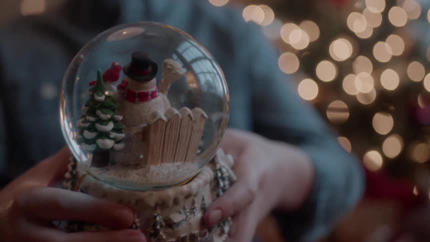 Boy holds a snow globe next to a christmas tree