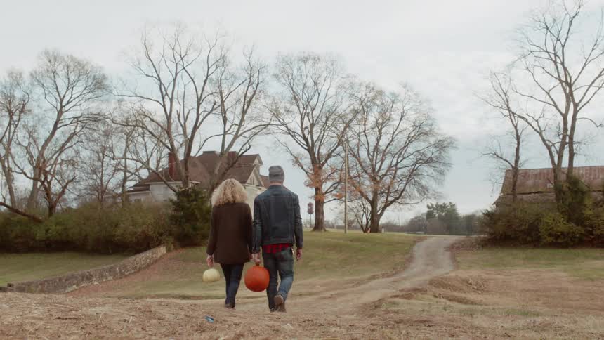 Man and woman walk towards a barn carrying pumpkins