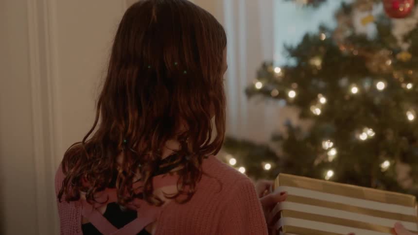 A boy and girl look at a present next to a christmas tree