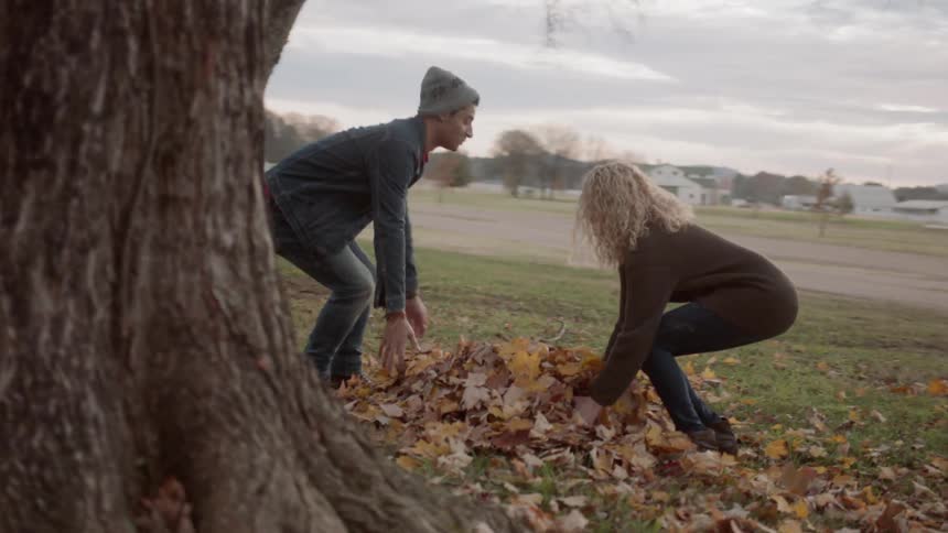 Man and woman run to a leaf pile and toss leaves