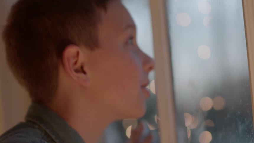 A boy watches snowfall from a window