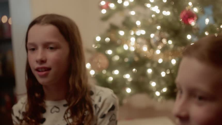 A boy and girl sit next to a christmas tree