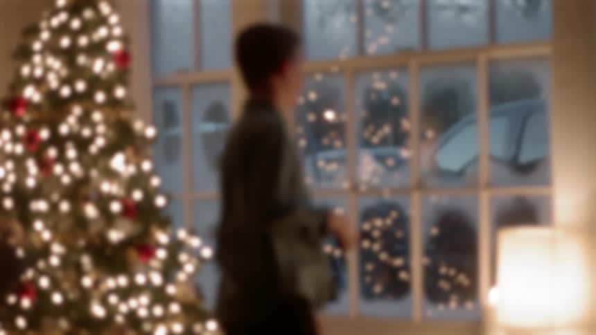 A boy runs past the christmas tree to look out the window
