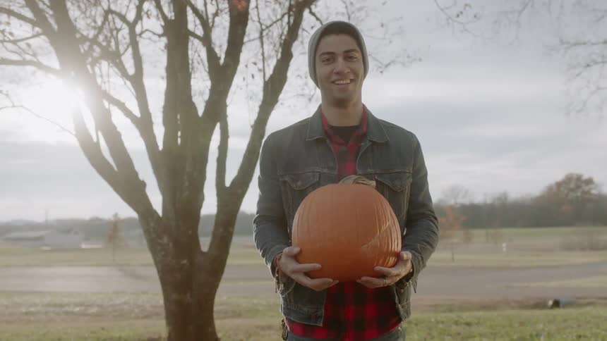 A man smiles while holding a large orange pumpkin