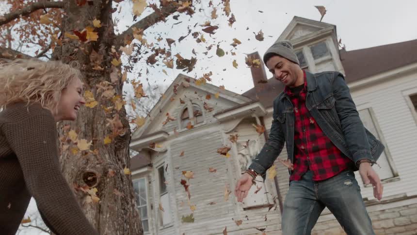Man and woman throw autumn leaves in the air