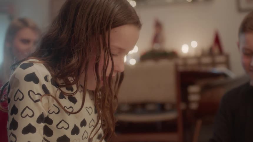Children are unwrapping gifts inside a home while their mother watches