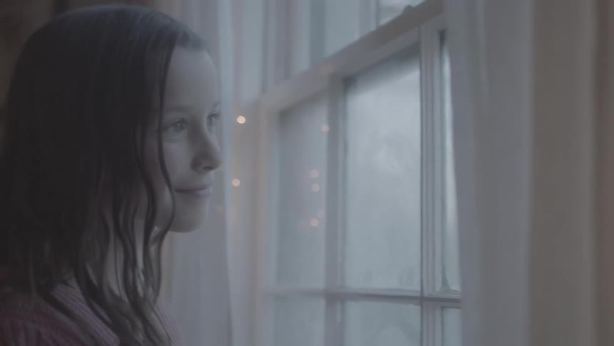 Girl looks outside a window to see it is snowing at christmas time