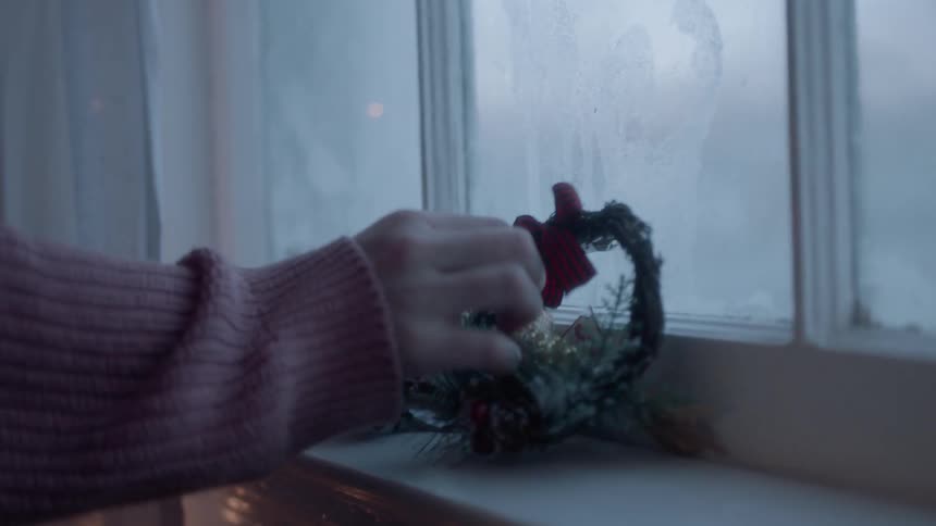 Person places mistletoe, small wreath, and candle on a window ledge