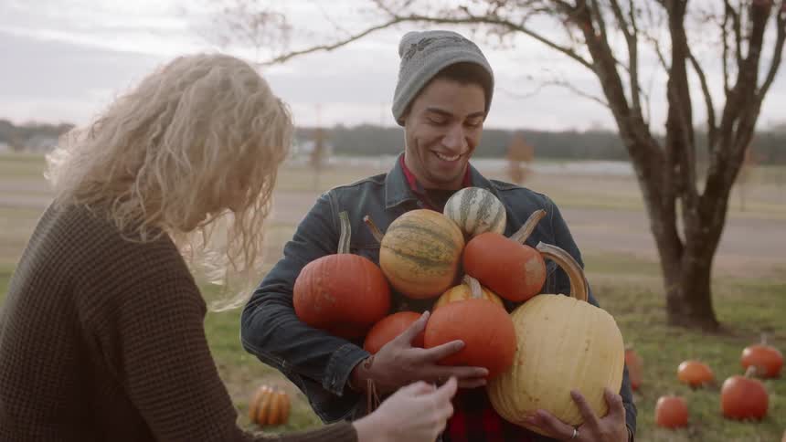 A woman helps stack a large quantity of pumpkins in a mans arms