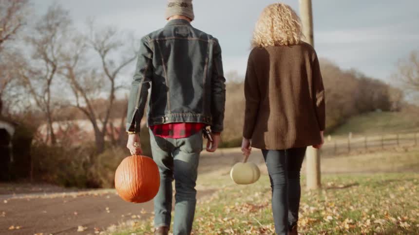 Couple carrying pumpkins on a cloudy fall day