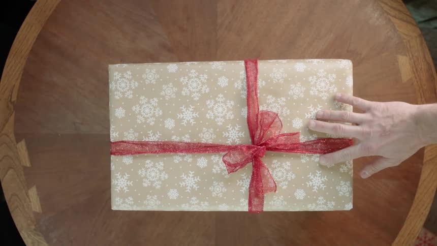 Hands place and remove a wrapped gift from a table