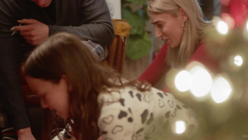 A family smiles as they sit on the floor near the tree