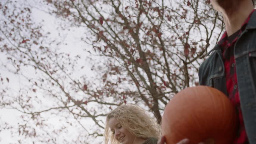 A woman picks up a pumpkin the walks away with a man