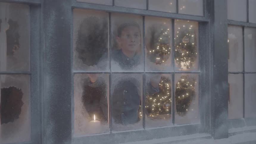 Boy looks outside a window to see it is snowing at christmas time