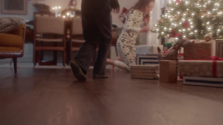 Brother and sister in pajamas run to the tree on christmas
