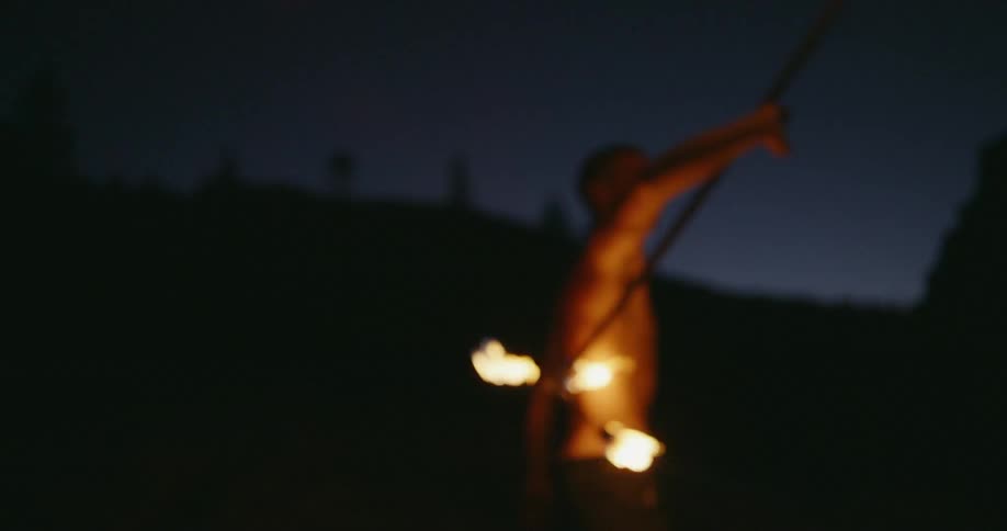 Man twirls a stick with fire on both ends outside at night