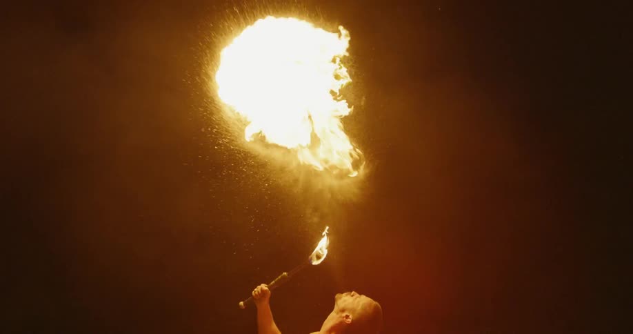 A man is creating large fire balls by breathing fire into a torch