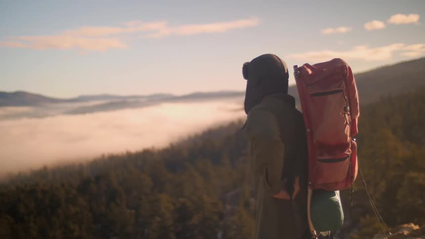 Man puts on hiking pack before a large forest