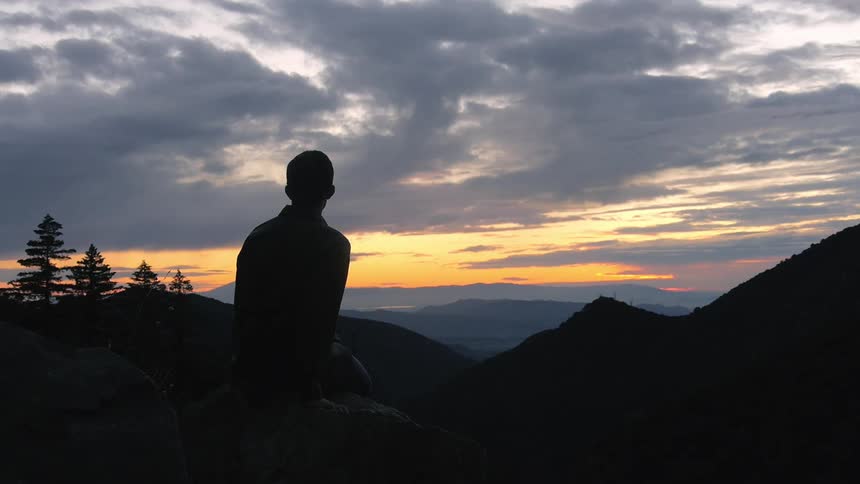 A  man sits on a rock on a mountain at sunset