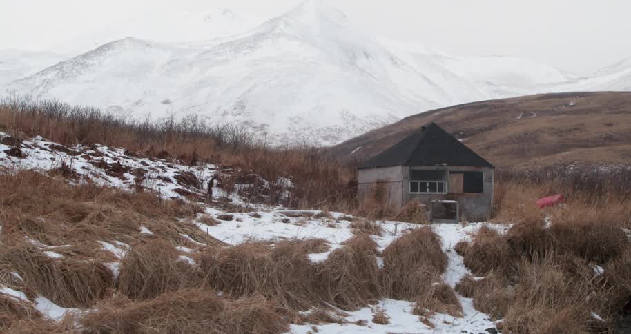 A small cabin sits in snowy mountains