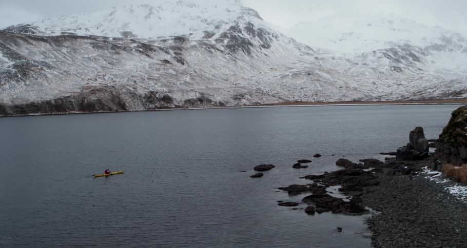 A person kayaks on a snowy mountain bay