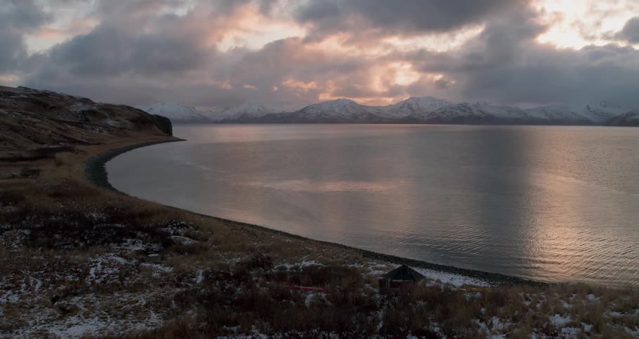 A calm sea with snow covered mountains in the background