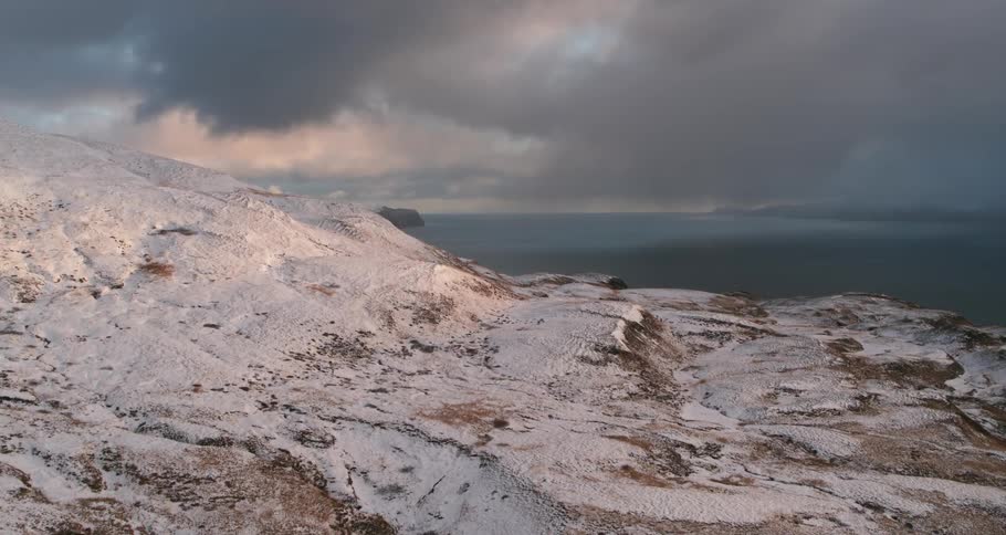 Storm clouds are hanging in the sky above snow-covered hills