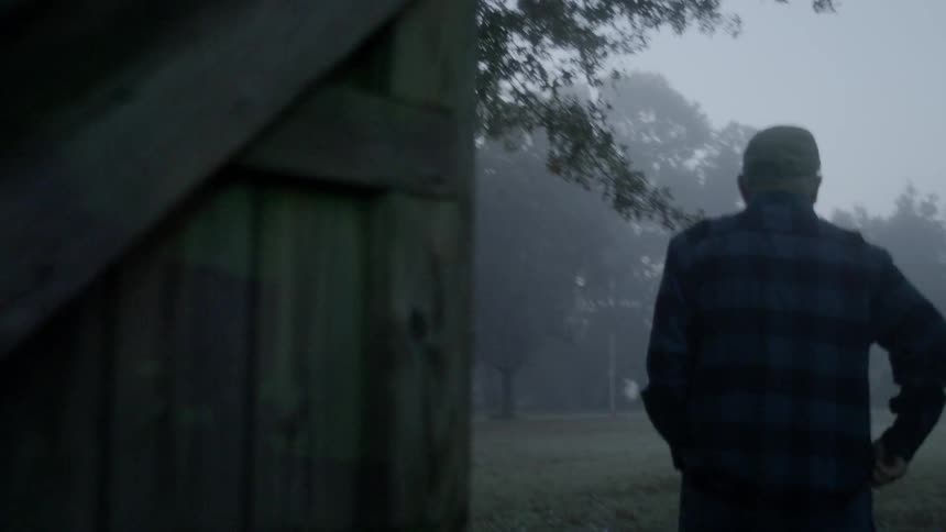 Man exits a rural barn on a foggy day