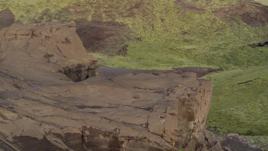 A cliff side is surrounded by a green meadow