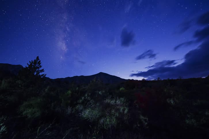 Stars and clouds move in the sky as dusk turns to night in the desert
