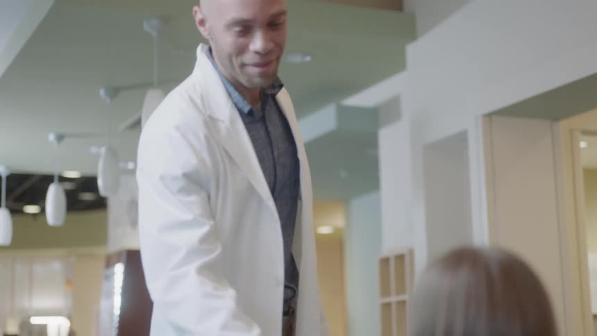 A doctor carrying a clipboard greets a patient