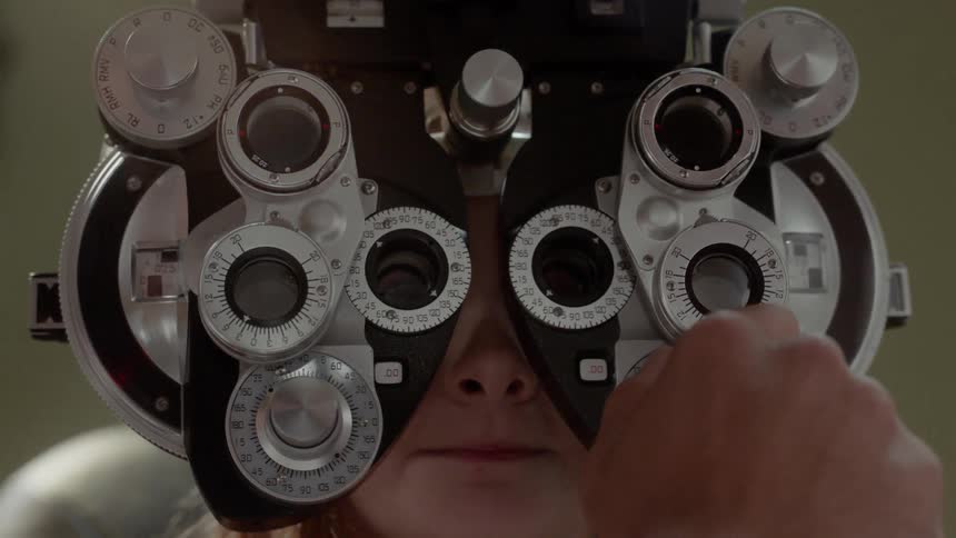 An optometrist is using a phoropter as he checks a girl's eyes