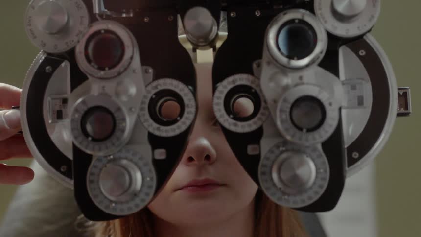 An phoropter is placed in front of a girl's eyes as she has an eye exam