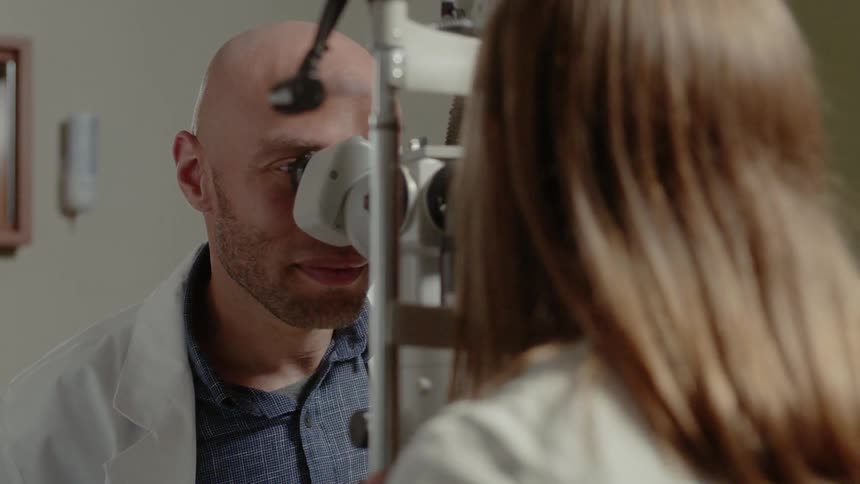 An eye doctor instructs a patient where to put their chin on the testing equipment