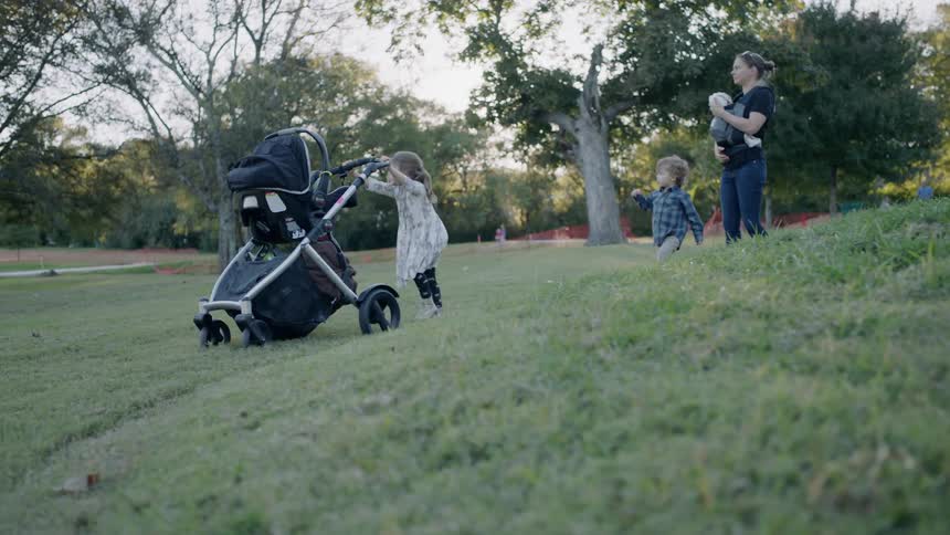 A little girl is pushing a stroller as she walks in a park with her family