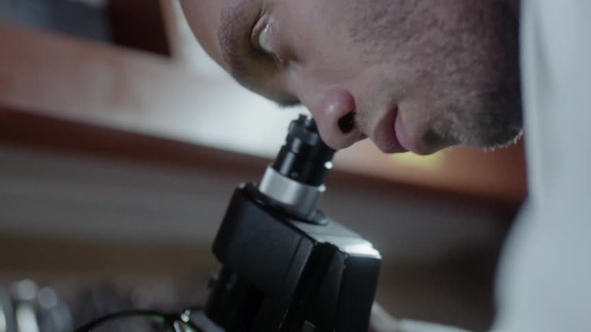 A man is looking into a microscope at a pair of eyeglasses