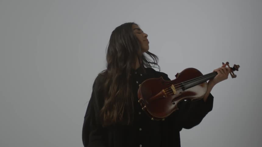 A woman standing in a room is raising a violin and preparing to play