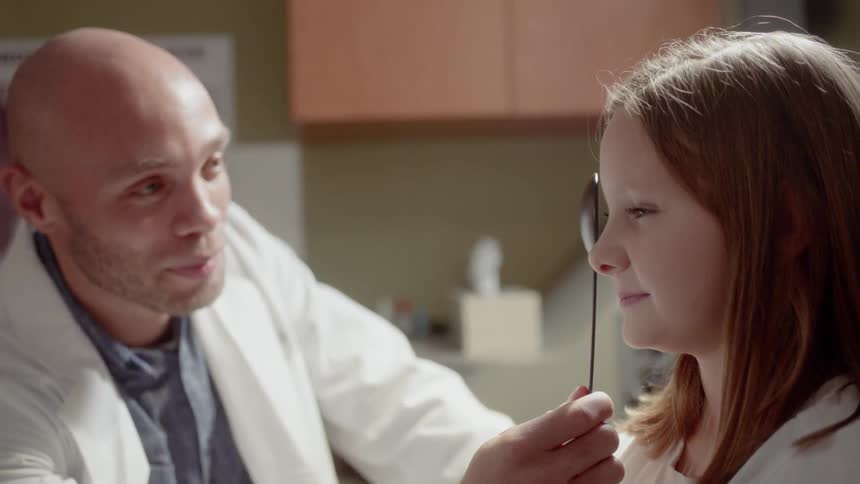A male eye doctor holds an object over a girl's eye during an eye exam