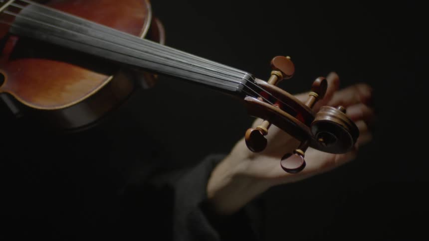 Woman adjusting the strings on her violin with a dark background