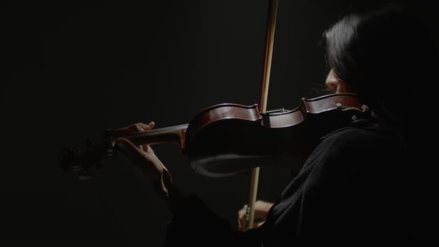 A woman plays a violin in a dark room