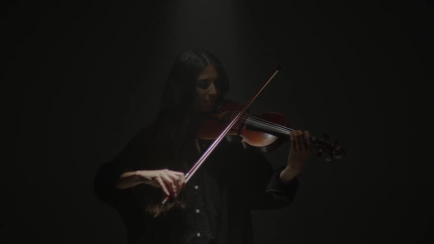 A woman plays a violin in a dark room