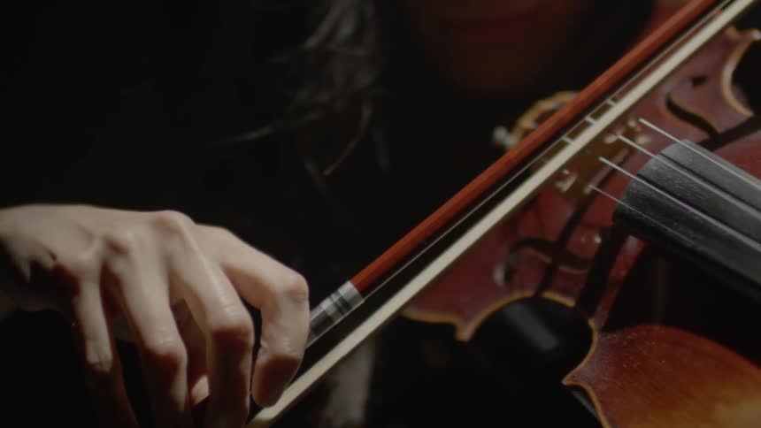 A woman slowly plays violin in the dark