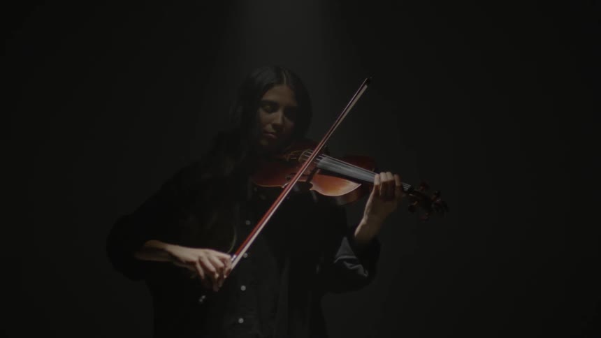 Woman plays violin in a dimly lit room