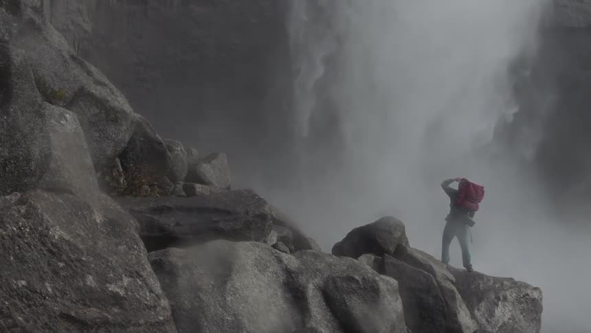 A hiker observes a waterfall on an overcast day