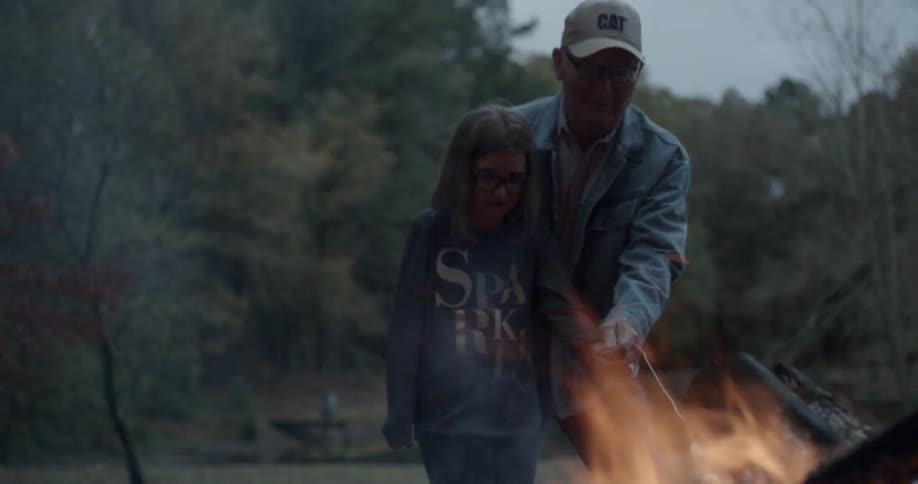 An old man and young girl are roasting a marshmallow at a campfire
