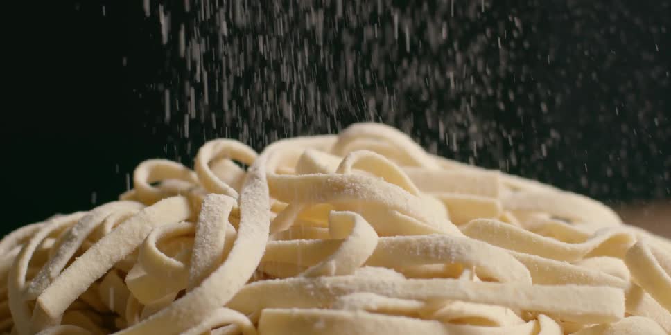 Flour is sprinkled on a pile of uncooked fresh pasta