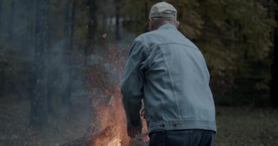 A man is building a large fire next to a forest